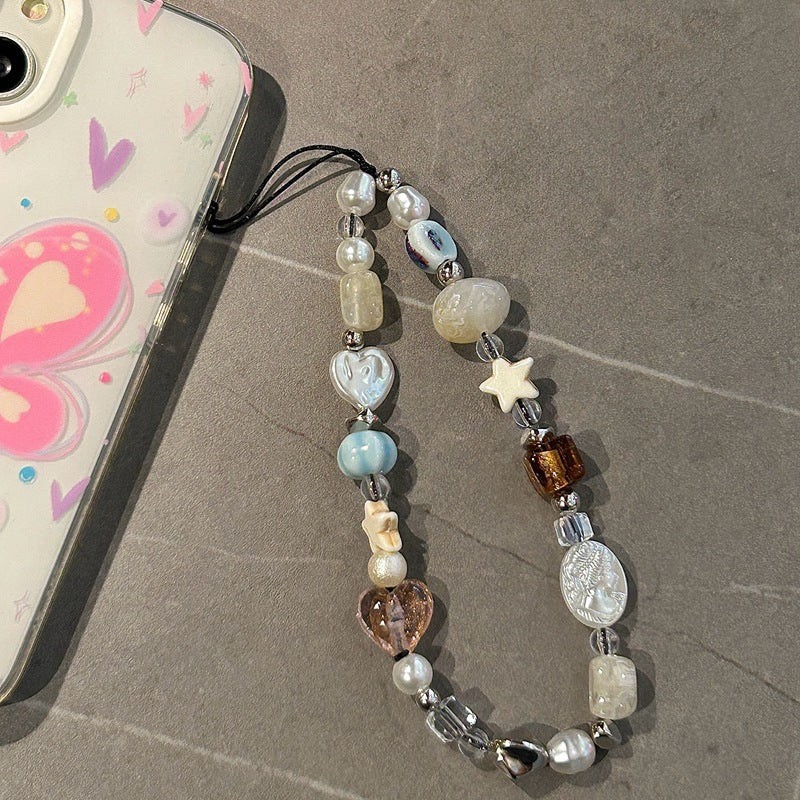 Crystal beaded phone lanyard, phone wrist strap with pearls, quartz, heart and star charms, attached to a phone case with pink butterfly design on a gray surface