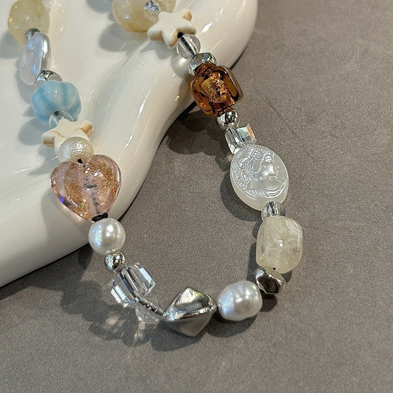 Crystal beaded phone lanyard, phone wrist strap with pearls, quartz, heart and star charms, attached to a phone case with pink butterfly design on a gray surface