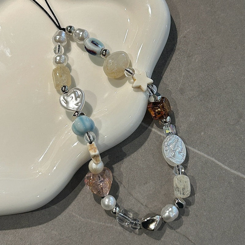Crystal beaded phone lanyard, phone wrist strap with pearls, quartz, heart and star charms, attached to a phone case with pink butterfly design on a gray surface