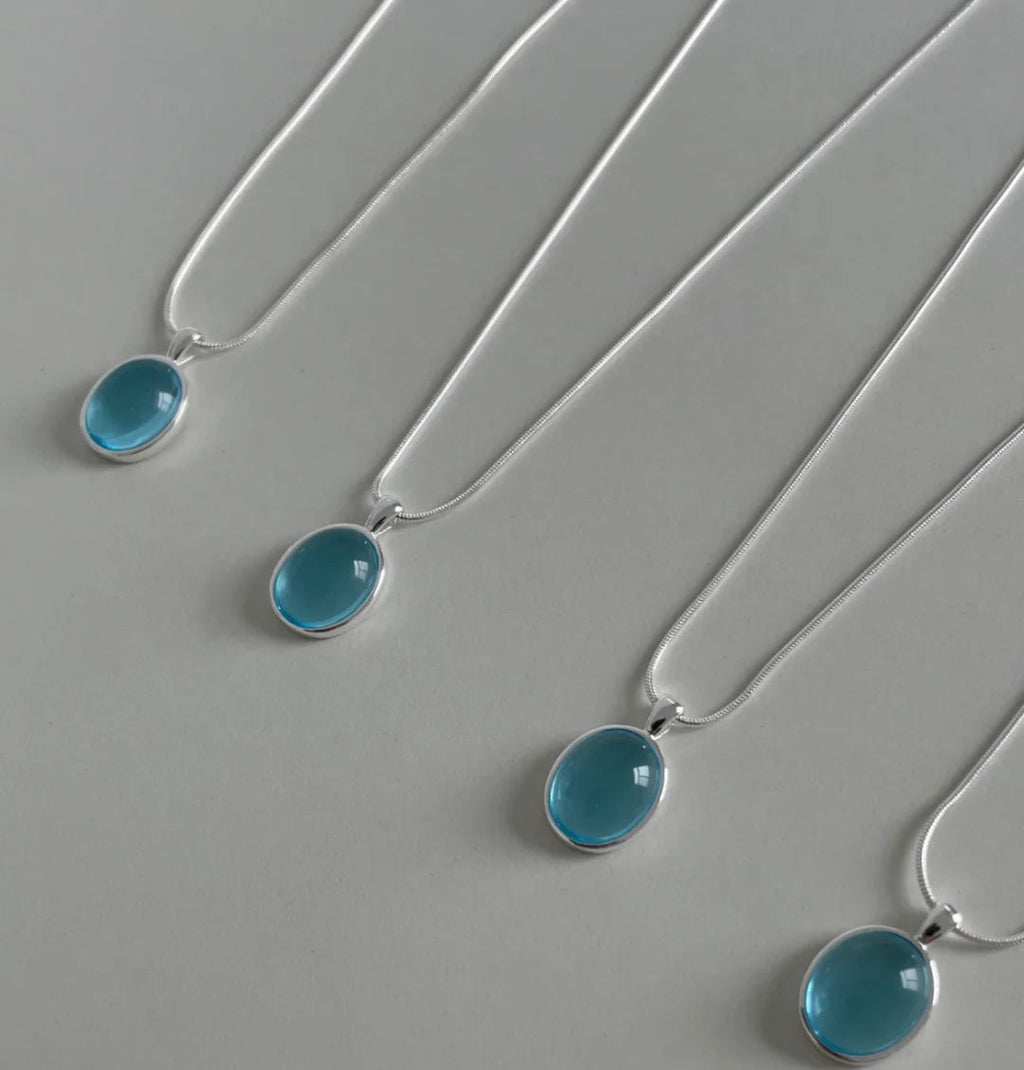 Three silver necklaces with blue pendants on a gray background