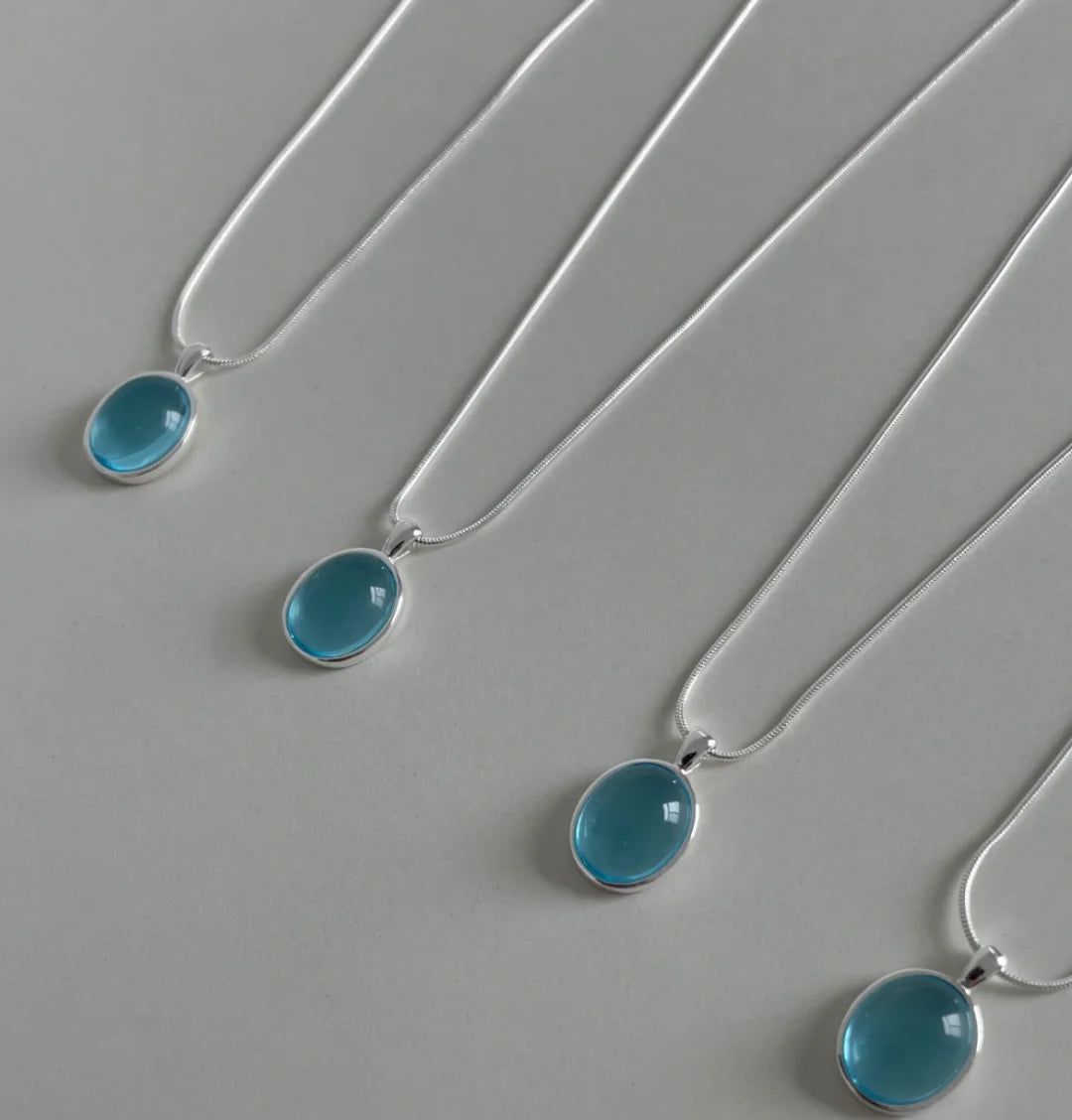 Three silver necklaces with blue pendants on a gray background