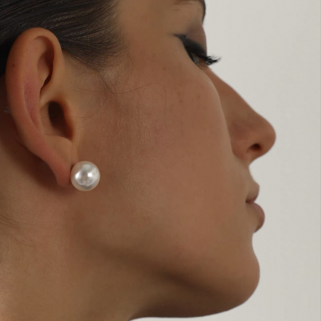 Close-up of a person wearing a pearl earring on a neutral background